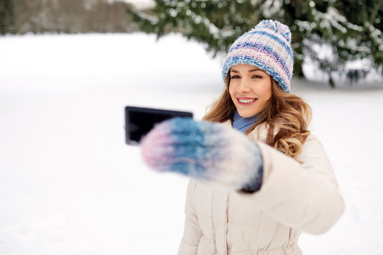 people, season and leisure concept - happy smiling woman taking selfie by smartphone in winter
