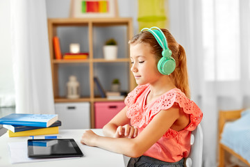 Fototapeta na wymiar children, education and technology concept - student girl in headphones with tablet computer at home desk