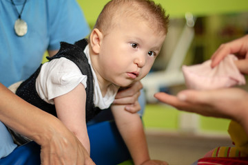 Portrait of a baby with cerebral palsy on physiotherapy in a children therapy center. Boy with disability has therapy by doing exercises. Little kid has musculoskeletal therapy in rehabitation centre.