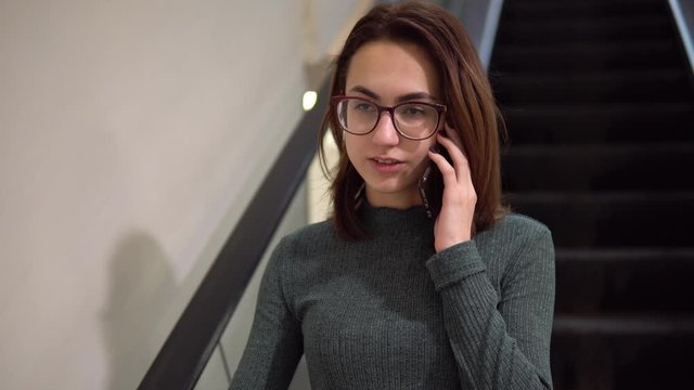 A young woman rides on an escalator and speaks on the phone. Large shopping center