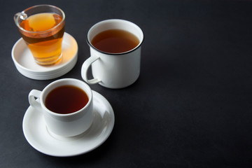 Three cups with hot tea drink on dark background, copy space. Tea time or tea brake. Autumn beverage. Toned image with tea cups.
