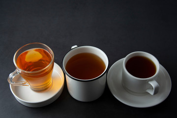 Three cups with hot tea drink on dark background, copy space. Tea time or tea brake. Autumn beverage. Toned image with tea cups.