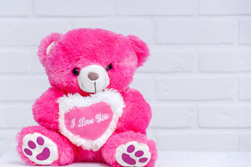A pink toy bear sits on a table against a white loft. Toy bear close-up. Holiday Greeting Card. Holiday background.