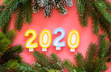 2020 New Year design. Date laid out by candles near fir branches on pink background top view