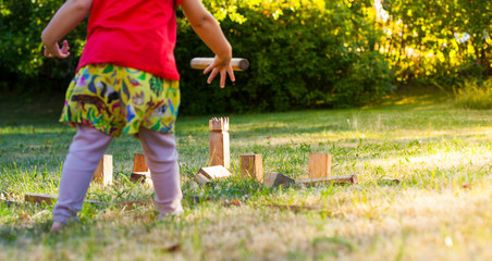 Mädchen spielt Wikingerschach (Kubb). Girl playing Kubb in garden.
