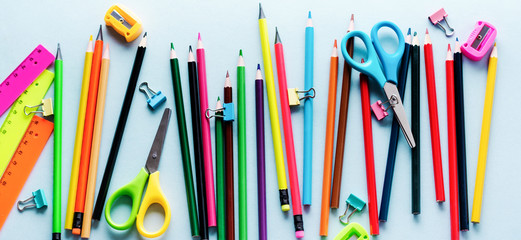 Colored pencils, scissors, notebook, ruler, pen, eraser, sharpener and more in glass. School and office stationery on light blue background. Concept back to school. Top view.