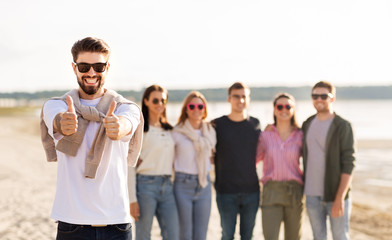 friendship, leisure and people concept - happy man with group of friends on beach in summer showing thumbs up