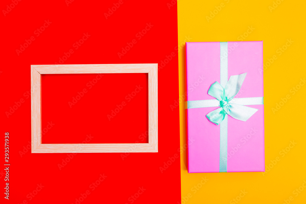 Poster gift box with ribbon together with a wooden frame on a colorful background. view from above.