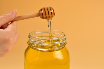 Dipper with honey in woman hand on orange background. Space for text or design.