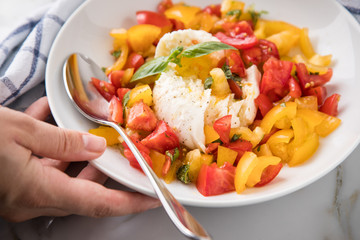 Frau isst Mozzarella Kugel mit roten und gelben Tomaten, Basilikum und Olivenöl auf Teller und  Marmor Hintergrund