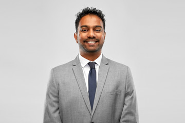 business, people and corporate concept - smiling indian businessman over grey background