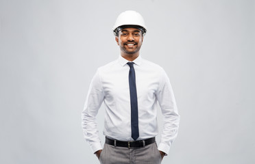 architecture, construction business and people concept - smiling indian male architect in helmet over grey background