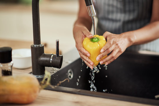 Close up of mixed race woman in apron standing in kitchen ad washing yellow paprika in sink.