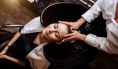 Gorgeous cute young woman enjoying head massage while professional hairdresser applying shampoo her...