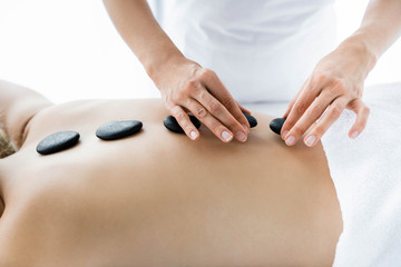 cropped view of masseur doing hot stone massage to woman in spa