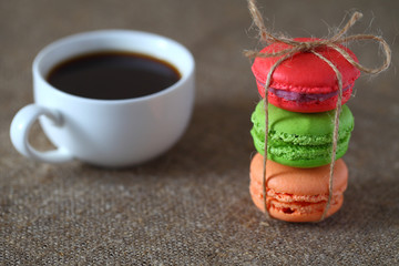 Macaron three pieces red, green and orange tied with rope and a mug of coffee on burlap tablecloth.