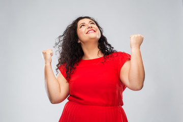 emotion, gesture and success concept - happy woman in red dress looking up and making fist pump over grey background