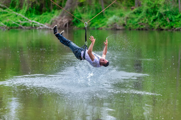 young man flying down on zipline over the river, extreme sport