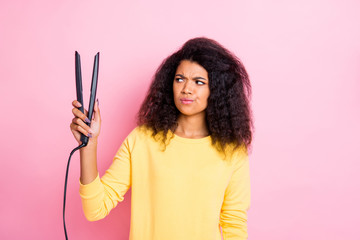 Portrait of minded pensive afro american girl hold look hair straightener think will it be good feel unsure wear yellow clothes isolated over pink color background