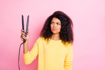 Obraz premium Portrait of minded pensive afro american girl hold look hair straightener think will it be good feel unsure wear yellow clothes isolated over pink color background