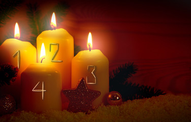 Four burning Advent candles with golden decoration and white snow.