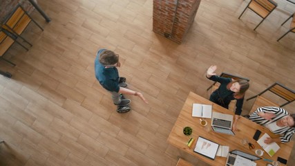 Top View of Late Employee on Self-Balancing Hoverboard Scooter Coming to Startup Loft Office and Greeting Coworkers by High Five. Overhead Team Work of Diverse Group of People. 4K Gimbal Panning Shot
