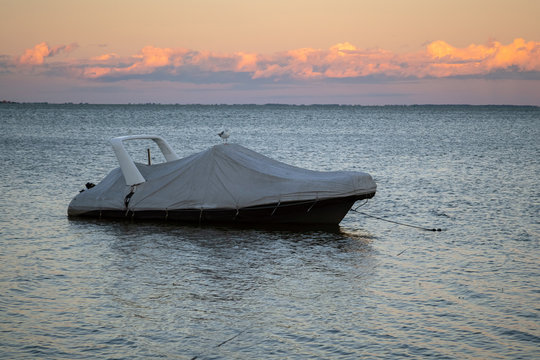 Covered boat docked at the pier by the shore at sunset. Covered yacht on the water with colourful sunset sky in the background