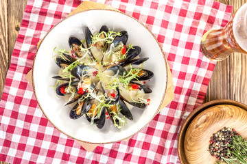 Cooked fresh mussels on white plate with glass of beer on wooden table