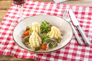 beef stroganoff with mashed potatoes and pickles with glass of red wine on wooden table