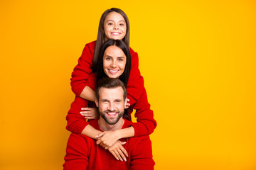 Photo of cheerful day charming fun funky positive family in red sweaters piggyback hugging each other smiling toothily enjoying spending free time with each other isolated vivid color yellow