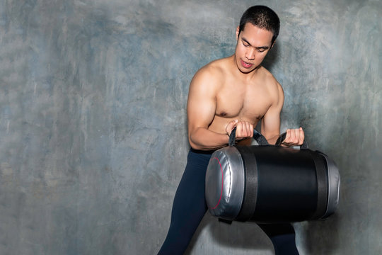 Perfect athletic Asian man training with power bag at gym.