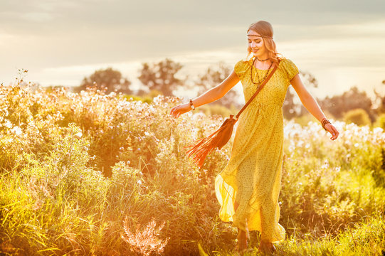 Smiling bohemian girl in yellow dress with guitar dance on the field at sunset warm light