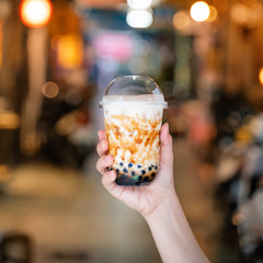 Young woman is holding, drinking brown sugar flavored tapioca pearl bubble milk tea with glass...