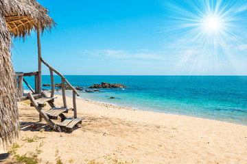 View of sand beach, sea, sun on blue sky and bungalow on tropical island