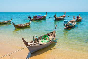 Fototapeta na wymiar Rows of many traditional wooden fishing long tail boats moored at tropical sand beach with rocks