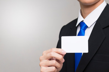 Business card in the hand of business people. Man wearing a black suit. There is copy space on the left.
