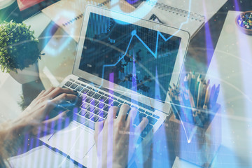 Double exposure of man's hands writing notes with laptop of stock market with forex graph background. Concept of research and trading.