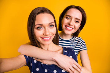 Close up photo of two amazing cute ladies making selfies hugging piggyback wear summer casual trendy t-shirts isolated yellow background