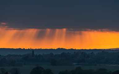 A heavy rain cloud dramatically lit by the setting sun over Warwickshire, England.