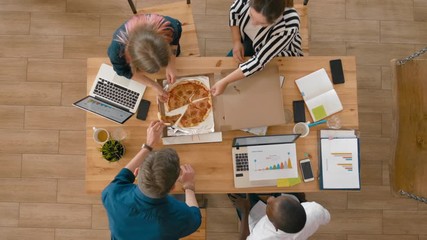 Top view of Lunch in Loft Office. Business Team of Hungry Young People Enjoy Eating Pizza Together. Food Delivery Service and Catering at Work. Overhead 4K Pull Out Gimbal Shot