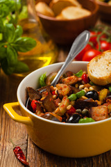 Traditional Italian caponata, served with croutons in a yellow, sunny pot. Decorated with basil and pine nuts.