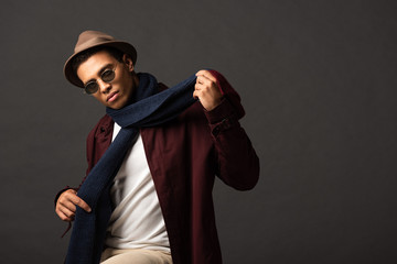 elegant mixed race man in scarf, sunglasses and hat on black background