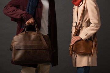 partial view of stylish couple in autumn outfit holding leather bags on black background