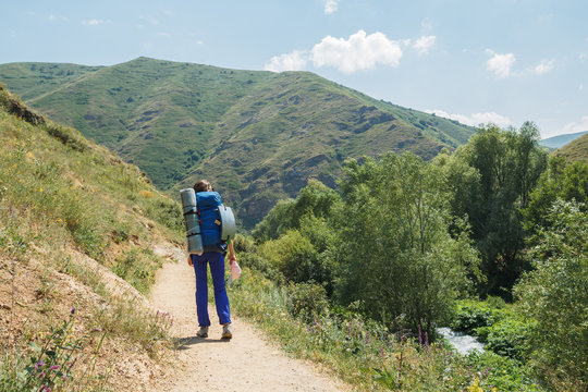 Traveling woman with backpack walking in mountainous area. Female traveler dressed in camping equipment walking along path.