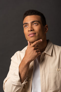 pensive handsome mixed race man in beige shirt looking away on black background