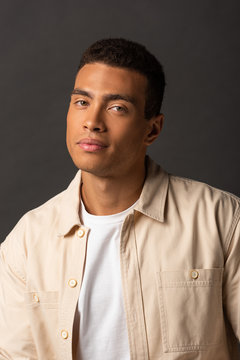 handsome mixed race man in beige shirt on black background