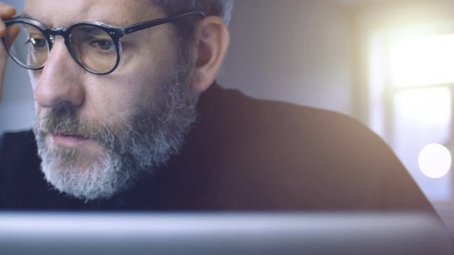 Businessman with glasses working on laptop computer in his office, thinking, reading and analyzing data media content