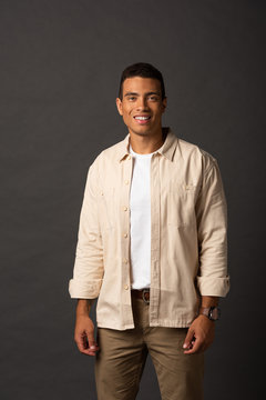 smiling handsome mixed race man in beige shirt on black background