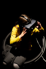 Virtual space.Girl sitting on the armchair in dark room and wearing virtual goggles, watching 360 virtual reality vision.