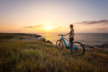 Fototapeta na wymiar Woman with a bike in the nature / Morning view of a woman with a bike enjoys the view of sunrise at the rocky Black Sea coast